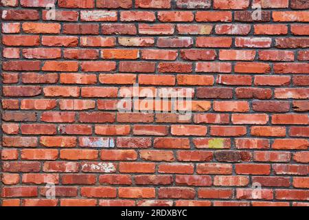 Many fading and chipped red bricks on wall with darkening mortar and blue and white paint splatter Stock Photo