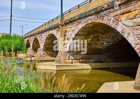 Gorgeous old stone bridge with stone arch underside and river flowing underneath in summer Stock Photo