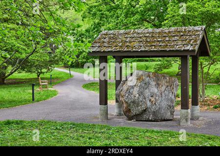 Wide shot of large boulder under moss covered roof in middle of park trail with distant bench Stock Photo