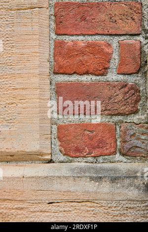 Textured tan colored concrete wall with rectangular red brick section background asset Stock Photo