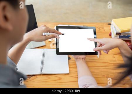 Mockup image of two student holding black tablet with blank desktop white screen while study at table in livingroom Stock Photo