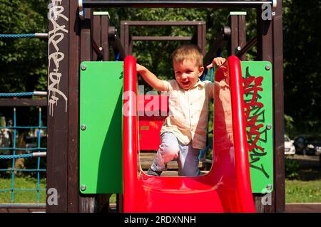 Little toddler playing on the playground and sitting on a slide Stock Photo