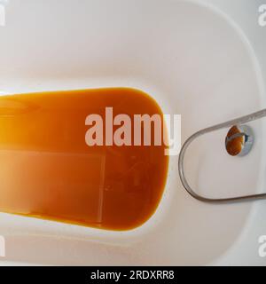 The bathtub is filled with dirty, rusty water from the drain.Bathing in the bathroom is unpleasant due to the presence of brown, rusty water. Stock Photo