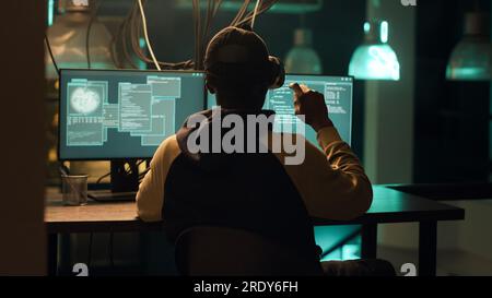 African american hacker using virtual reality glasses to hack computer server, creating malware and security breach to steal important information. Criminal doing hacktivism. Handheld shot. Stock Photo