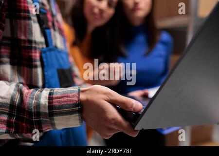 Storehouse employees using laptop while working in storage room. Warehouse asian managers and package handler team manaing order fulfillment with close up on portable computer Stock Photo