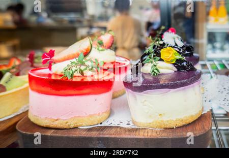 Strawberry and blueberry cheese cakes on display at a café. Unrecognizable waiter and customers in the background. Stock Photo