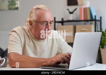Concentrated senior man in glasses working on laptop at home Stock Photo