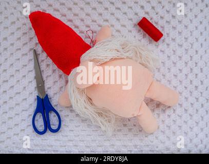 Scandinavian gnome with long beard red hat white knit background step by step handmade tutorial. Homemade fabric swedish Christmas decoration DIY. Hob Stock Photo
