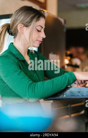 Young blond waitress cashing till at bar Stock Photo