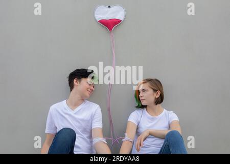 Teenage couple connected with IV drips in front of gray wall Stock Photo