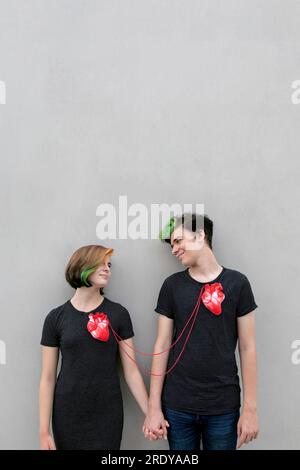 Teenage couple connected with hearts against gray background Stock Photo