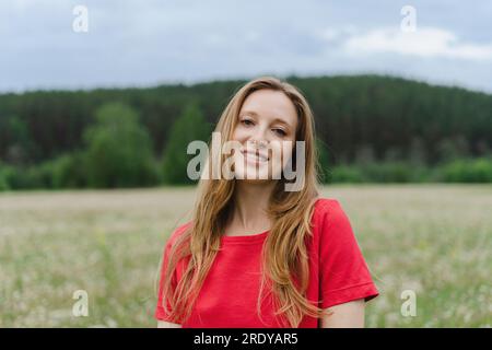 Smiling young woman wearing red t-shirt with blond hair on field Stock Photo