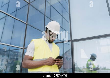 Engineer in reflective clothing text messaging on smart phone in front of glass building Stock Photo