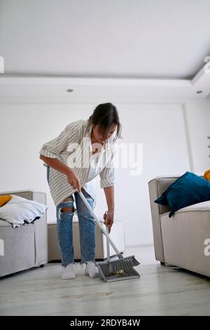 Woman cleaning with broom in living room at home Stock Photo