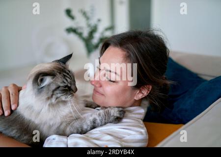Smiling woman with cat lying on sofa at home Stock Photo