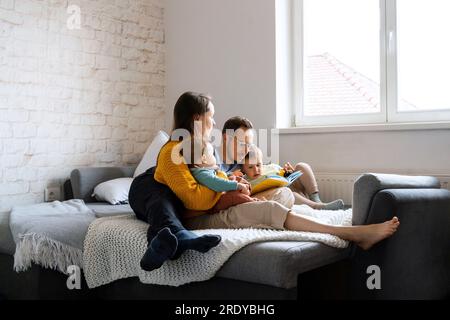 Parents reading book with children on couch at home Stock Photo