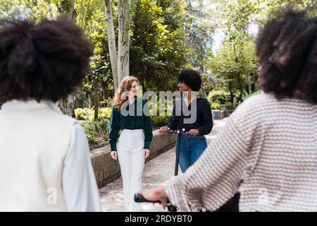Happy young woman riding electric push scooter and spending time with friends Stock Photo