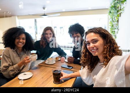 Happy woman taking selfie with friends and enjoying in cafe Stock Photo
