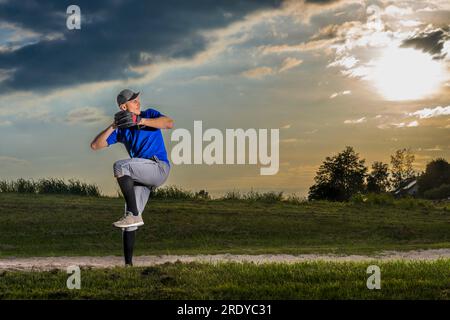 Young man playing baseball on grass at dusk Stock Photo