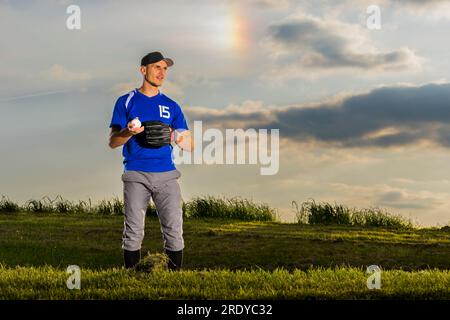 Man playing baseball on grass at dusk Stock Photo