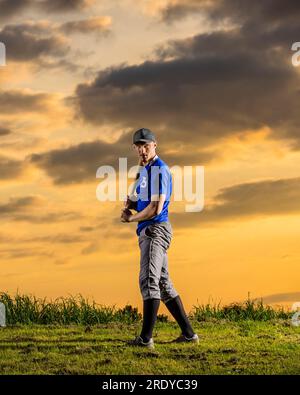 Young man holding baseball bat with sky in background at dusk Stock Photo