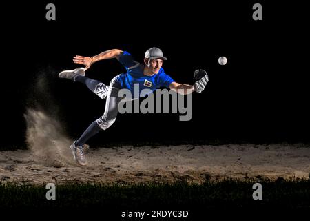 Young man wearing sports clothing catching baseball at night Stock Photo