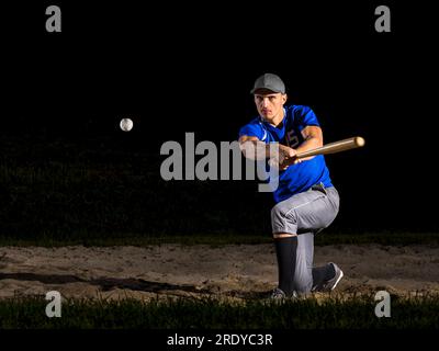 Young man hitting baseball with bat at night Stock Photo