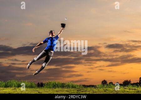 Young man jumping and catching baseball at dusk Stock Photo