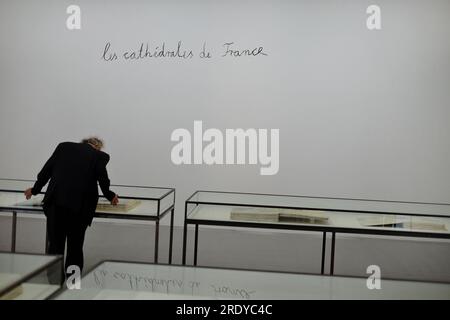 A man in a black suit looks at paintings in books in table vitrines, Les Cathédrales de France by Anselm Kiefer, KIEFER RODIN; 2017 at the Musée Rodin Stock Photo