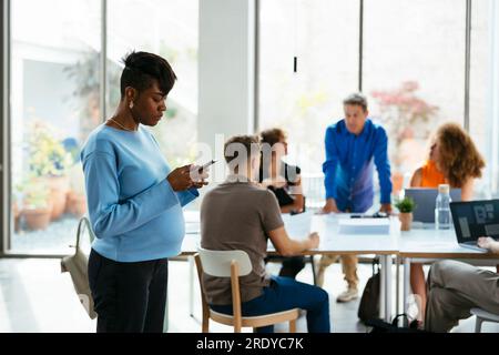 Businesswoman using smart phone with colleagues having discussion in background Stock Photo