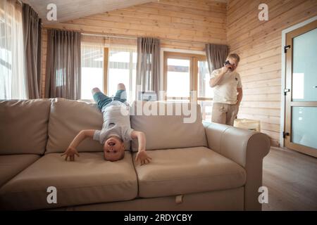 Son playing on sofa and father talking on phone at home Stock Photo