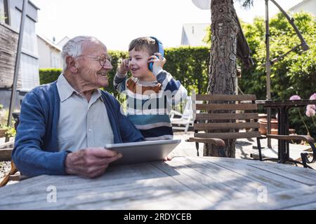 Smiling senior man with grandson wearing wireless headphones Stock Photo