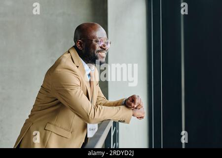 Smiling businessman in suit leaning on railing at convention center Stock Photo