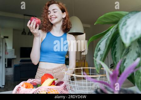 Happy young woman holding apple fruit in kitchen at home Stock Photo