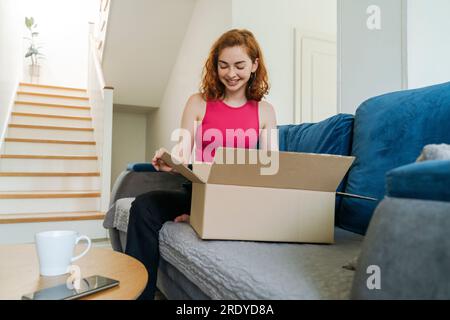 Happy young woman unboxing package on sofa at home Stock Photo