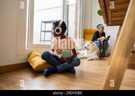 Thoughtful boy sitting with smart phone and looking through window at home Stock Photo