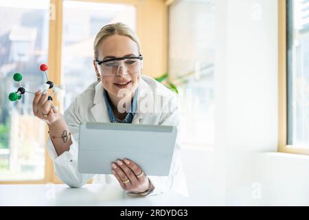 Scientist holding molecular structure and researching on tablet PC in laboratory Stock Photo