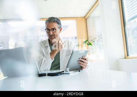 Mature man in lab coat using tablet PC in clinic Stock Photo
