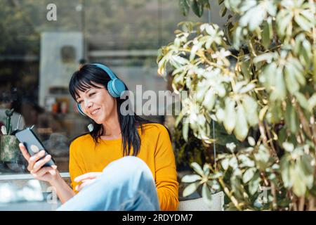 Happy woman wearing wireless headphones listening to music and using mobile pone Stock Photo