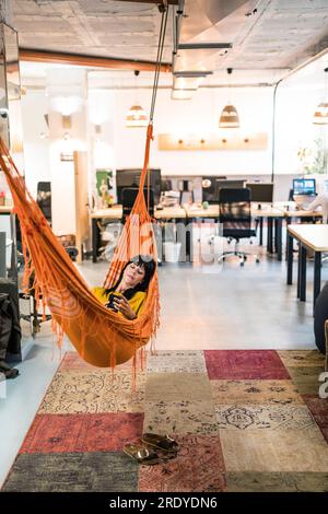 Businesswoman using smart phone and relaxing in hammock Stock Photo
