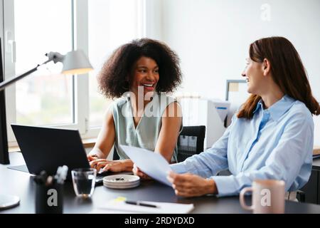 Happy colleagues talking and working at desk in office Stock Photo