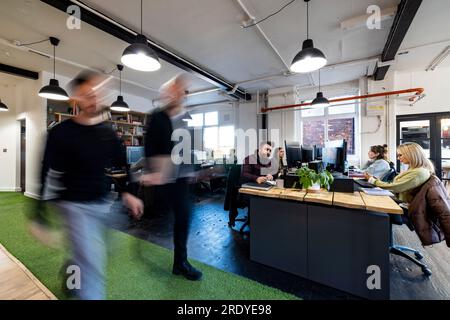 Businessmen walking with colleagues sitting at desk in office Stock Photo