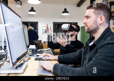 Businessman wearing virtual reality simulators with colleague working on desktop PC Stock Photo
