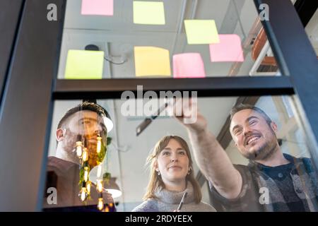Happy businessman with colleagues discussing over adhesive notes Stock Photo
