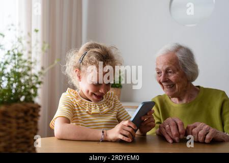 Smiling granddaughter using smart phone by grandmother at home Stock Photo