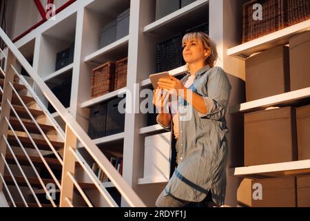 Thoughtful woman standing with tablet PC on staircase Stock Photo