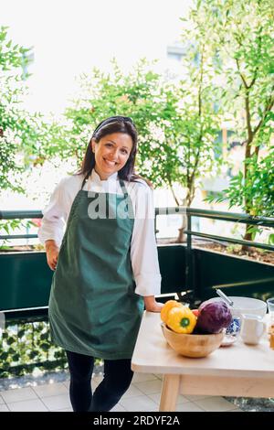 Smiling chef wearing apron leaning on table in balcony Stock Photo