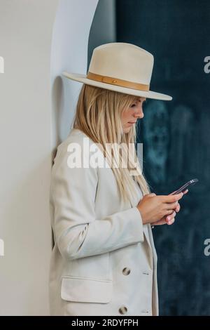 Blond woman using smart phone standing near wall Stock Photo