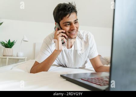 Smiling man lying on bed and talking on smart phone at home Stock Photo
