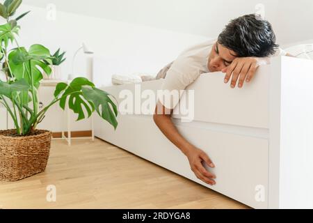 Tired man sleeping on bed next to potted plant Stock Photo